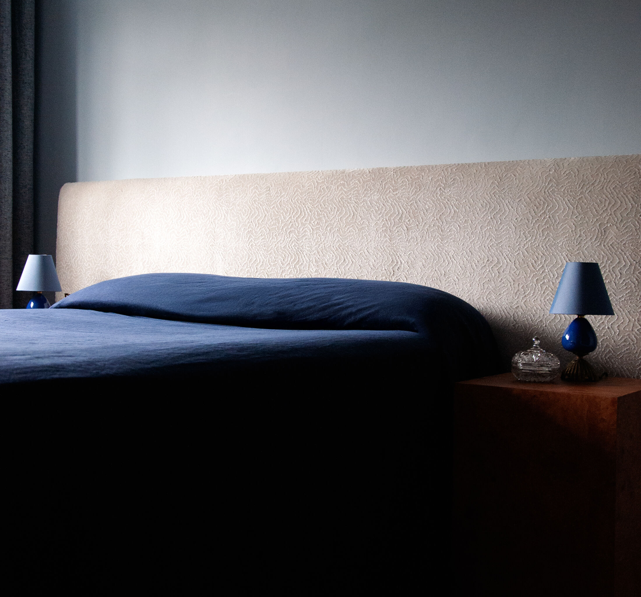 Bedroom with textured cream headboard, navy linen bedding and cobalt glass lamps