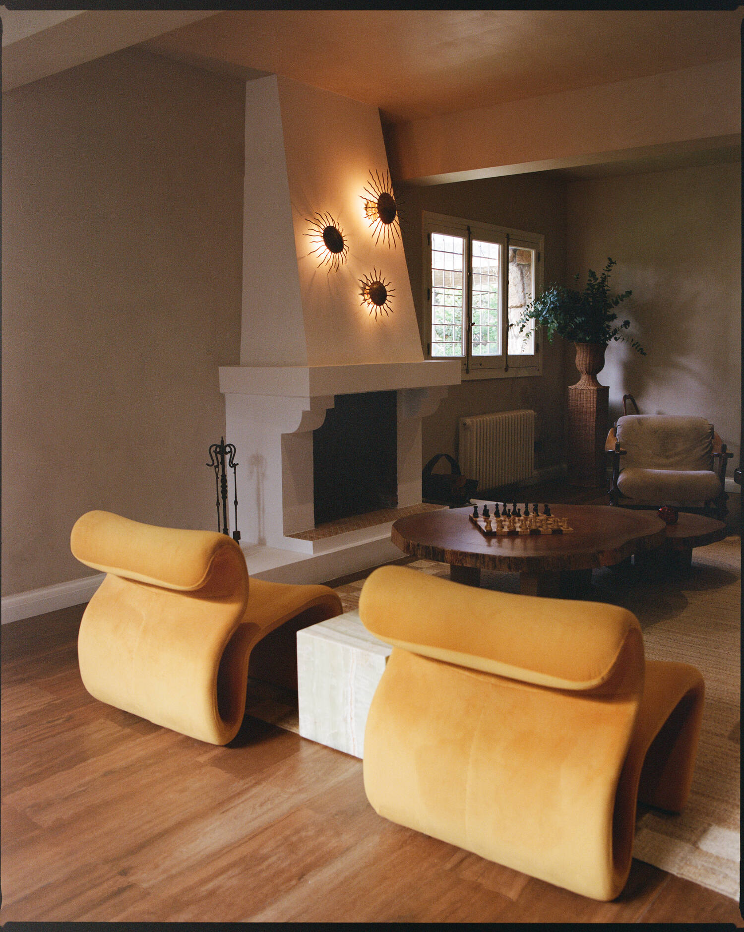 Sculptural ochre velvet chairs beside the plaster fireplace
