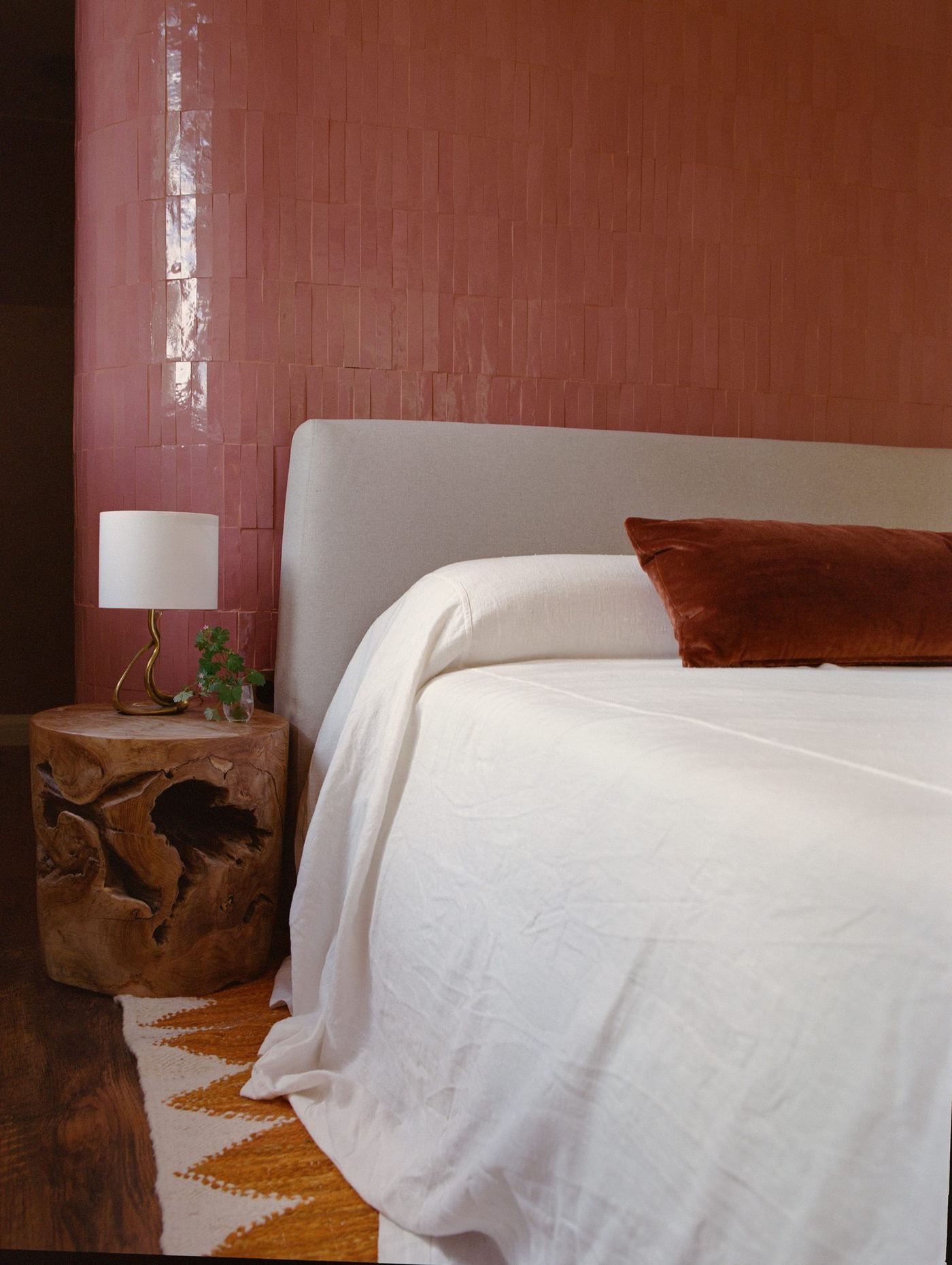 Bedroom with terracotta wall, white linen and a timber stool