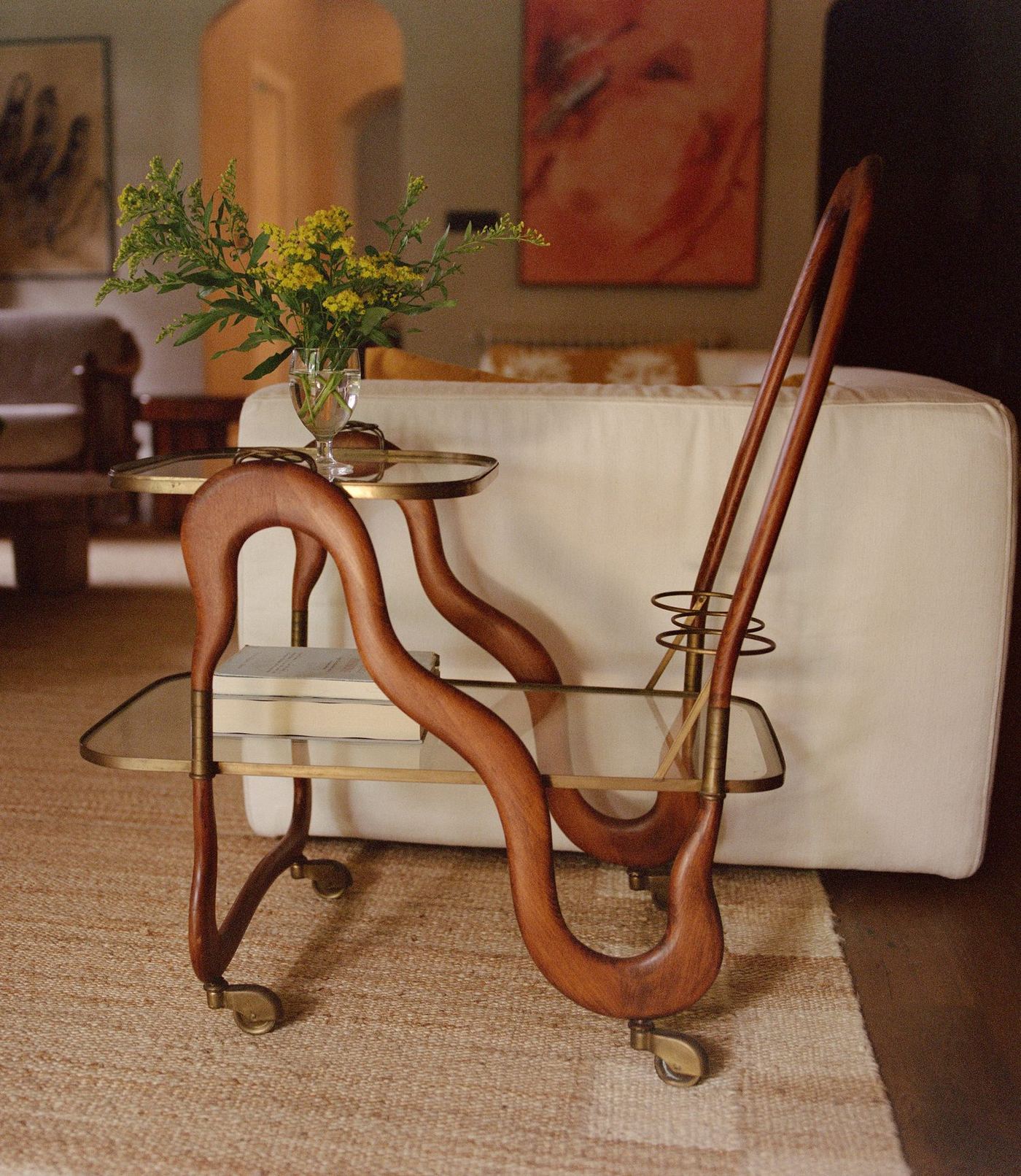 Sculptural timber bar cart beside a white sofa and artwork