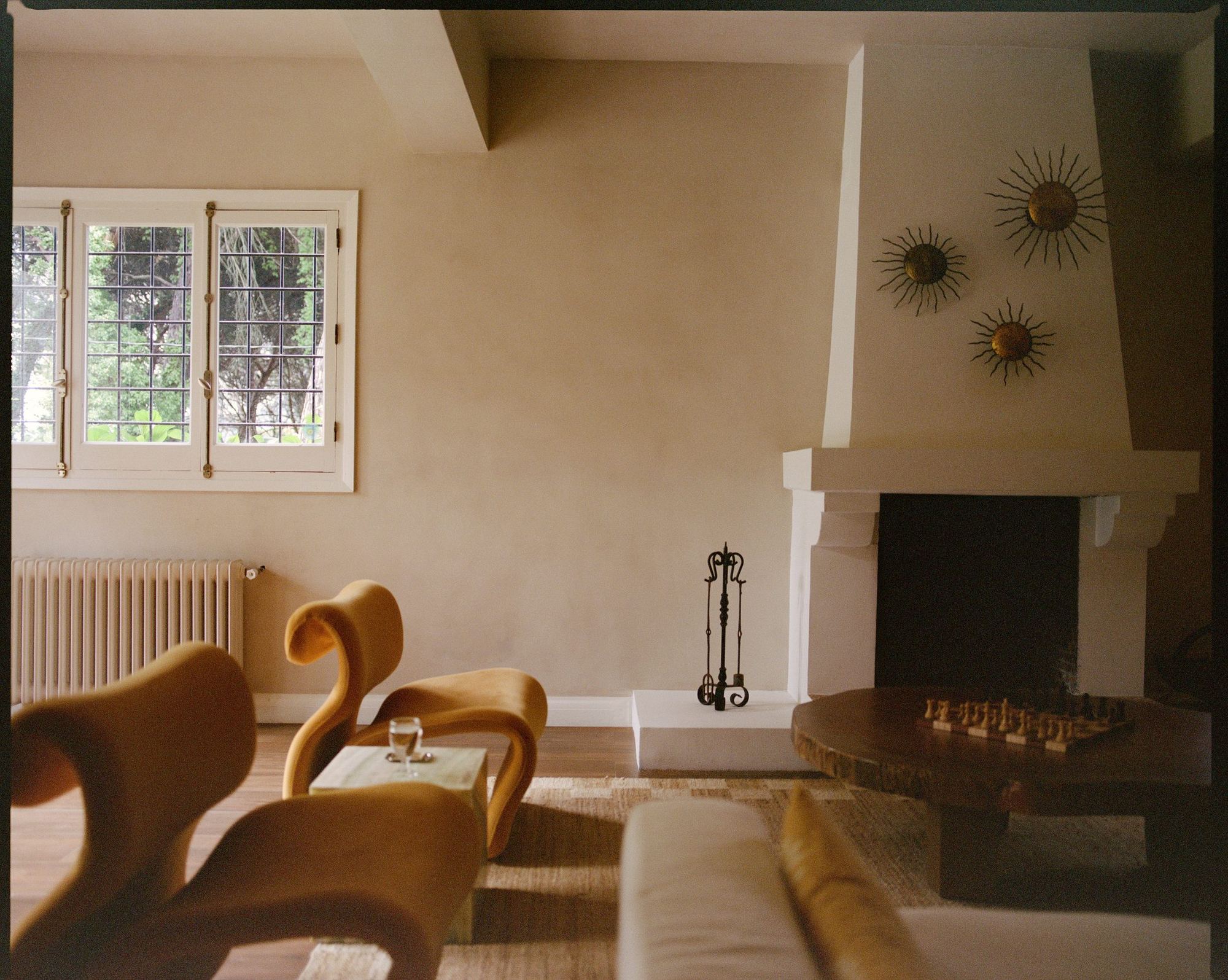 Living room with white plaster fireplace, gilded sun mirrors and sculptural chairs